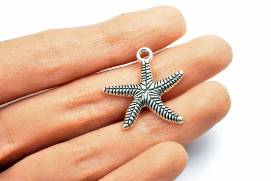 Silver starfish pendant charm held in hand.