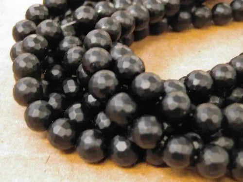 Black faceted round gemstone beads on beige surface.