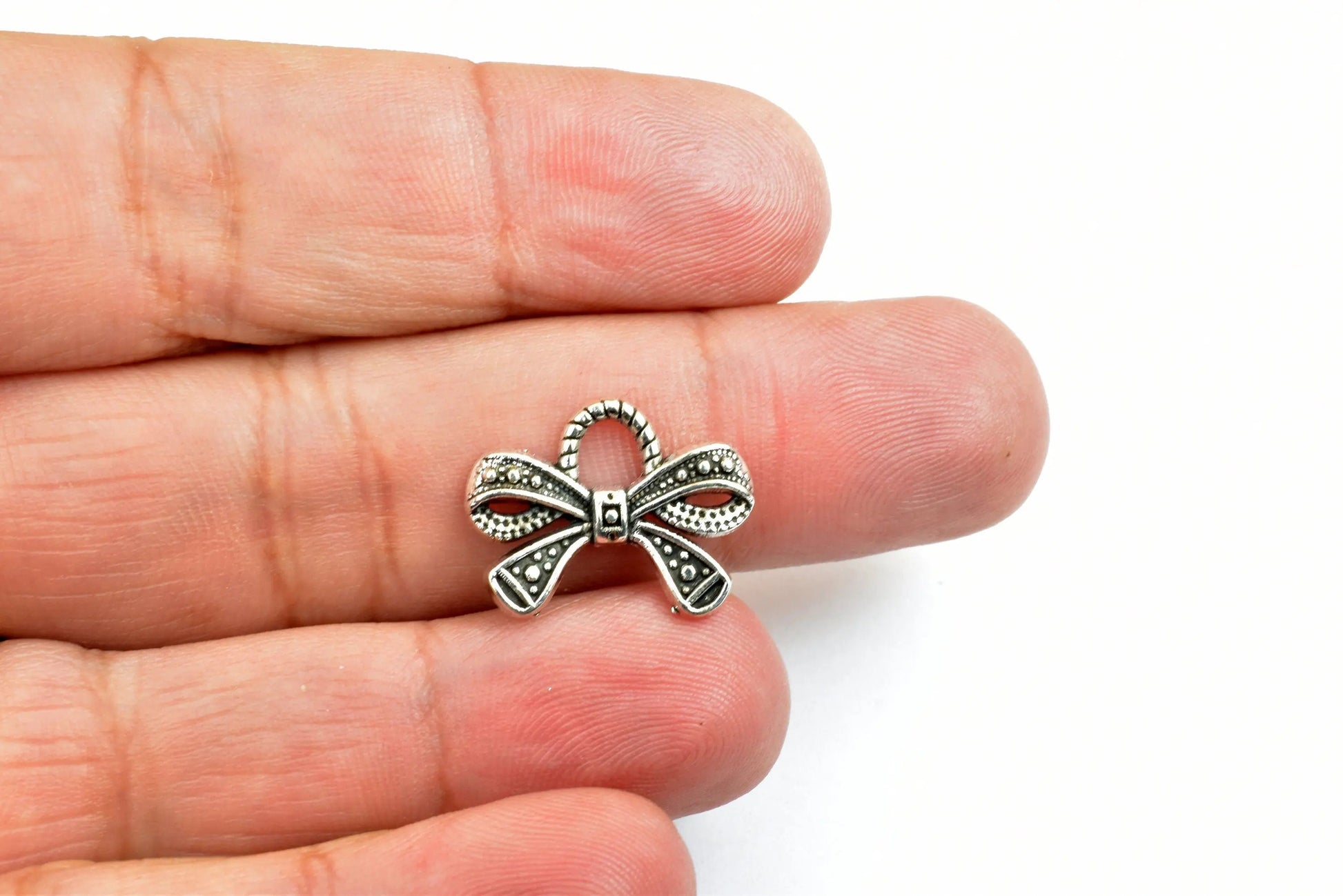 Silver bow-shaped charm with textured details held between fingers.