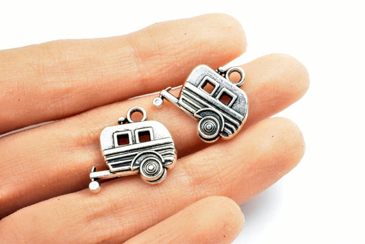 Vintage silver camper trailer charms displayed on fingers.