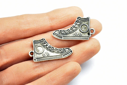 Silver sneaker charms on fingertips, shoe-shaped pendants for jewelry making.