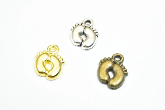 Three miniature baby feet charms in gold, silver, and bronze for jewelry making.