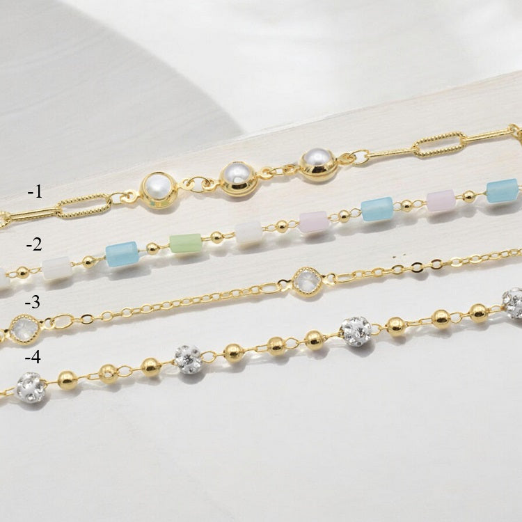 "Set of four gold delicate bracelets with pearls, colorful beads, and crystals on light background"