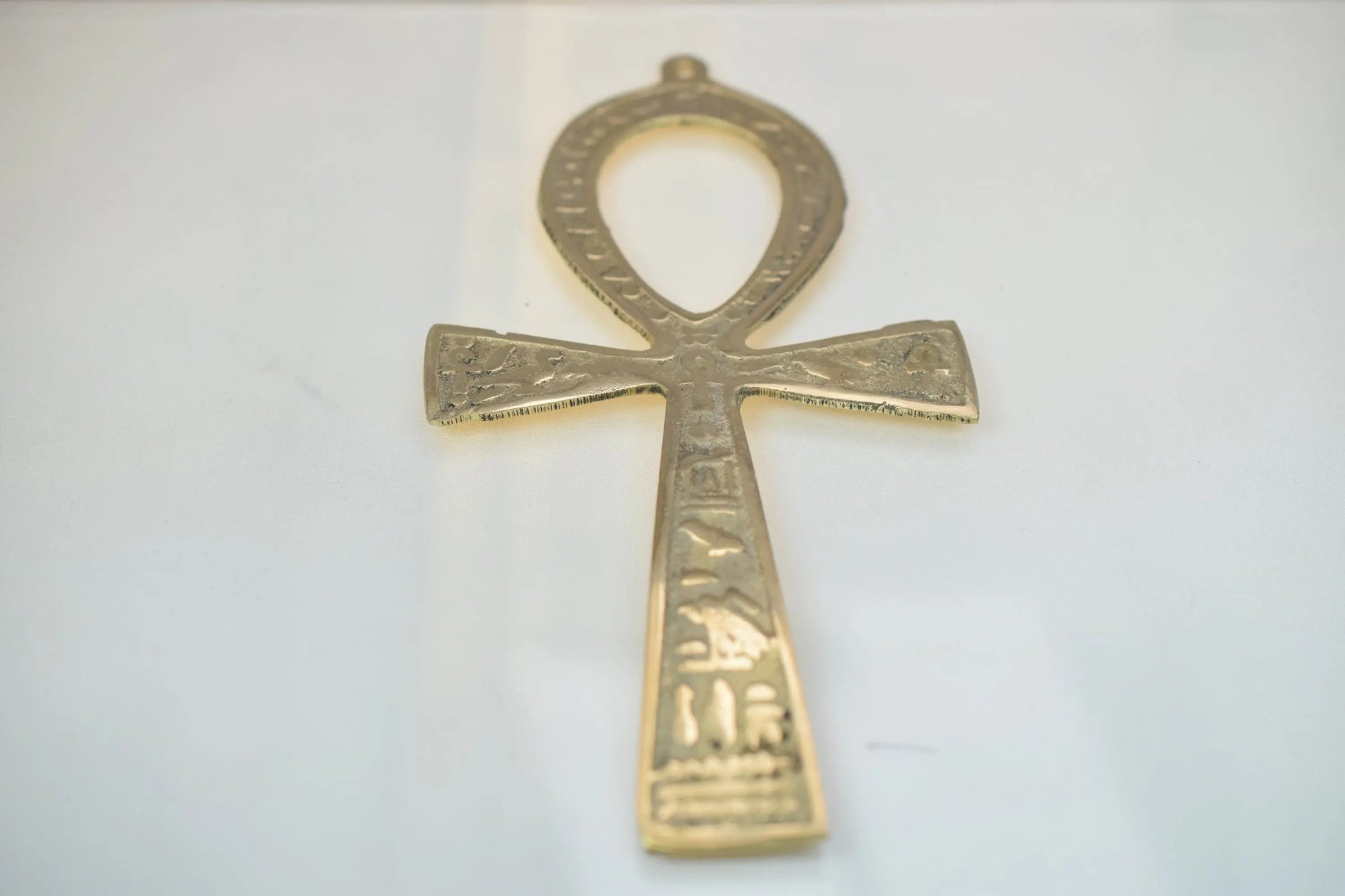 Golden Egyptian ankh symbol with hieroglyphs on white background.