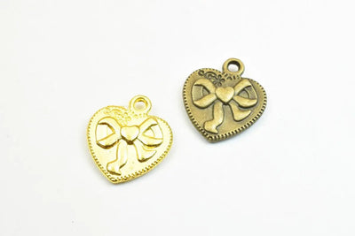 Heart-shaped metal charms with bow design in gold and bronze tones.