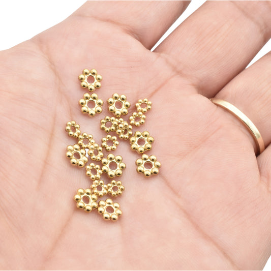 "Hand holding small gold flower bead spacers for jewelry making"