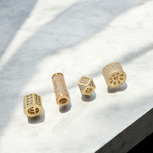 Gold cylindrical jewelry pieces with diamond embellishments on a marble surface.