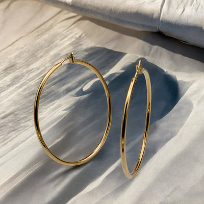 Close-up view of chunky gold hoop earrings with a polished finish, placed on a fabric background for an elegant look.