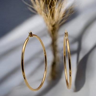 Close-up view of chunky gold hoop earrings with a polished finish, placed on a fabric background for an elegant look.
