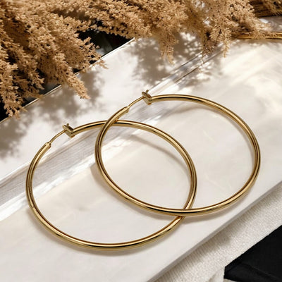 Close-up view of chunky gold hoop earrings with a polished finish, placed on a fabric background for an elegant look.