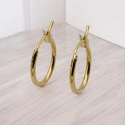 Close-up view of chunky gold hoop earrings with a polished finish, placed on a fabric background for an elegant look.