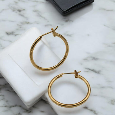 Close-up view of chunky gold hoop earrings with a polished finish, placed on a fabric background for an elegant look.