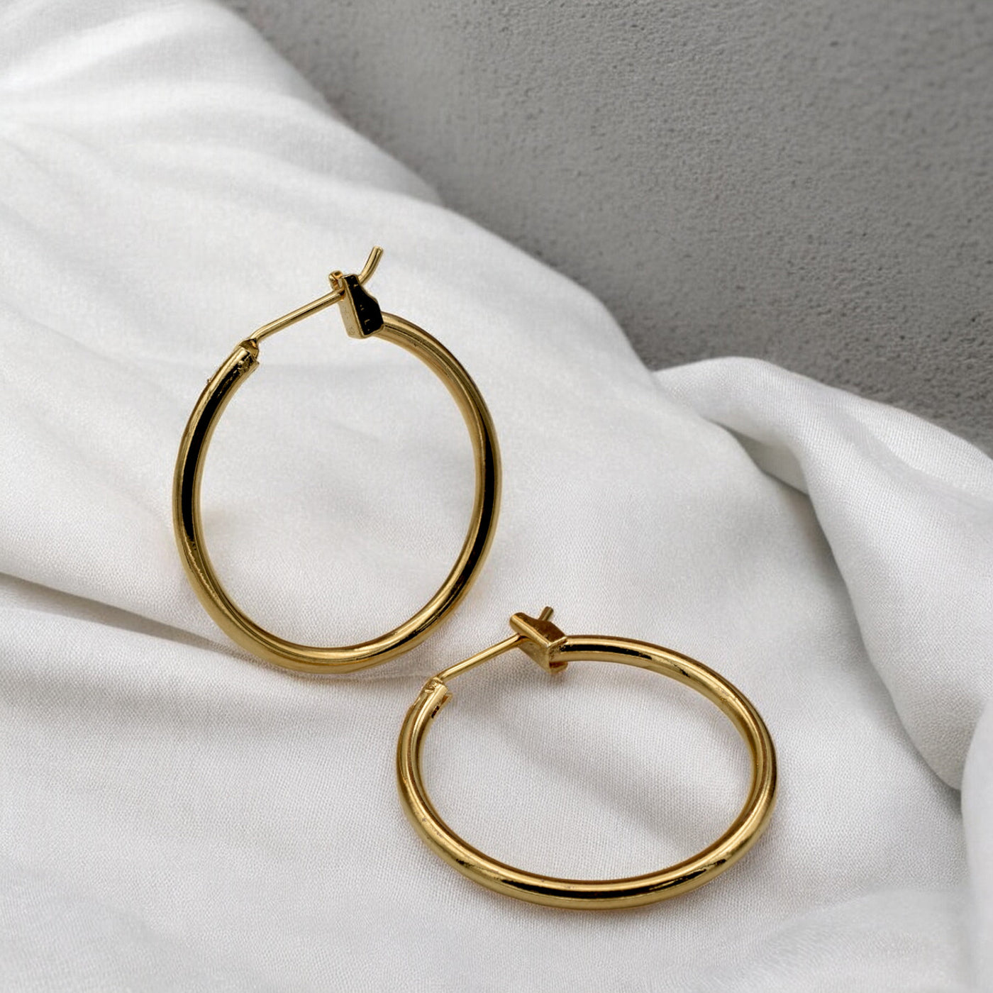 Close-up view of chunky gold hoop earrings with a polished finish, placed on a fabric background for an elegant look.
