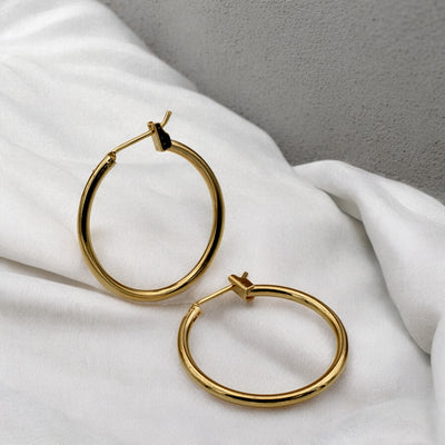 Close-up view of chunky gold hoop earrings with a polished finish, placed on a fabric background for an elegant look.