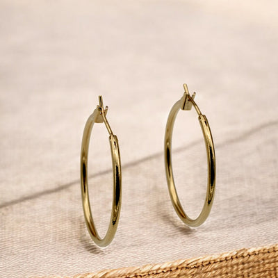 Close-up view of chunky gold hoop earrings with a polished finish, placed on a fabric background for an elegant look.
