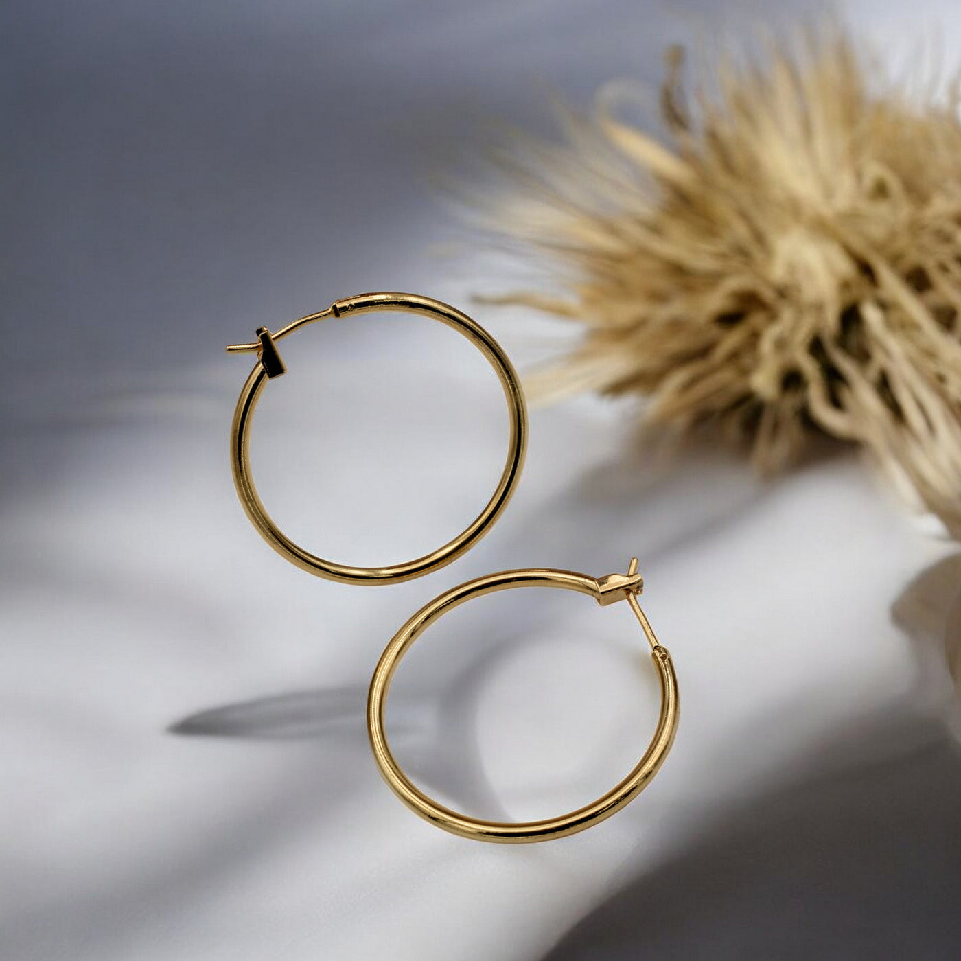 Close-up view of chunky gold hoop earrings with a polished finish, placed on a fabric background for an elegant look.