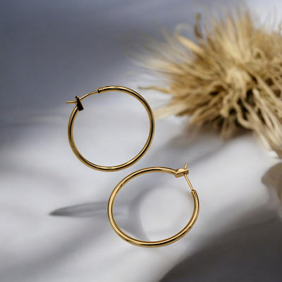 Close-up view of chunky gold hoop earrings with a polished finish, placed on a fabric background for an elegant look.