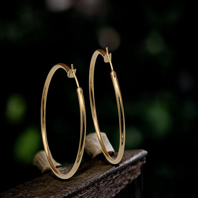 Close-up view of chunky gold hoop earrings with a polished finish, placed on a fabric background for an elegant look.