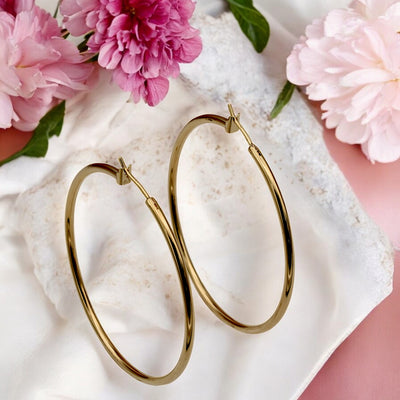 Close-up view of chunky gold hoop earrings with a polished finish, placed on a fabric background for an elegant look.