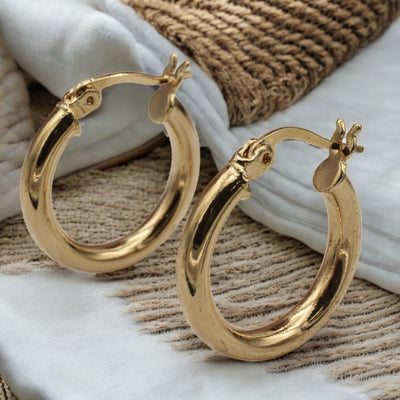 Set of gold hoop earrings in multiple sizes displayed on a black background, emphasizing their shiny, reflective surface and classic design.