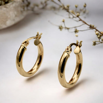 Set of gold hoop earrings in multiple sizes displayed on a black background, emphasizing their shiny, reflective surface and classic design.