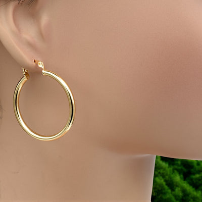 Set of gold hoop earrings in multiple sizes displayed on a black background, emphasizing their shiny, reflective surface and classic design.