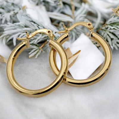 Set of gold hoop earrings in multiple sizes displayed on a black background, emphasizing their shiny, reflective surface and classic design.