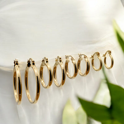 Set of gold hoop earrings in multiple sizes displayed on a black background, emphasizing their shiny, reflective surface and classic design.