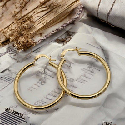Set of gold hoop earrings in multiple sizes displayed on a black background, emphasizing their shiny, reflective surface and classic design.