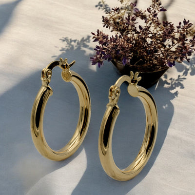 Set of gold hoop earrings in multiple sizes displayed on a black background, emphasizing their shiny, reflective surface and classic design.
