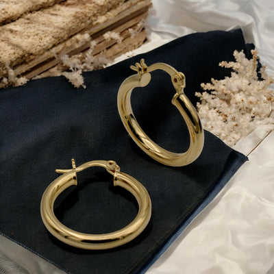 Set of gold hoop earrings in multiple sizes displayed on a black background, emphasizing their shiny, reflective surface and classic design.
