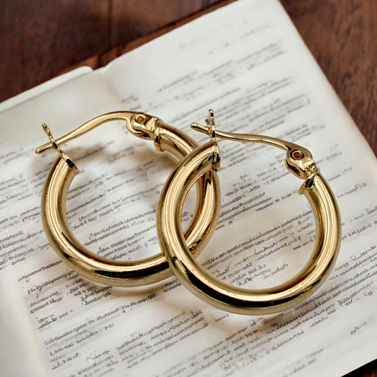 Set of gold hoop earrings in multiple sizes displayed on a black background, emphasizing their shiny, reflective surface and classic design.