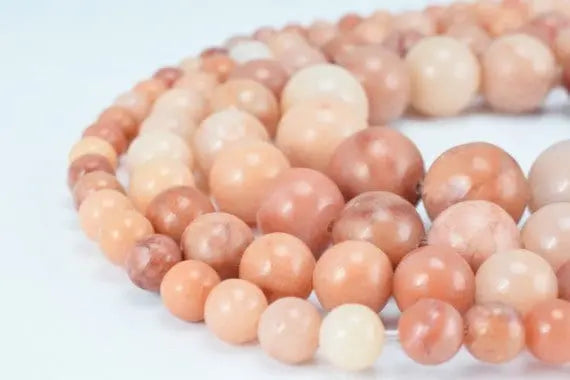 Polished pink and peach gemstone beaded necklace on white background.