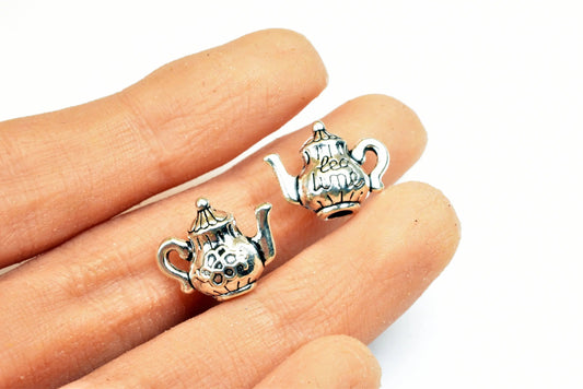 Miniature silver teapot charms held in hand for jewelry making.