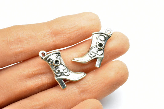 Silver cowboy boot charms on a hand, western-themed jewelry accessory.