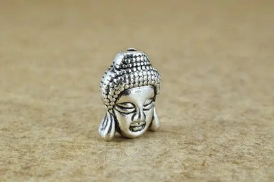 Silver Buddha head charm bead on beige background.