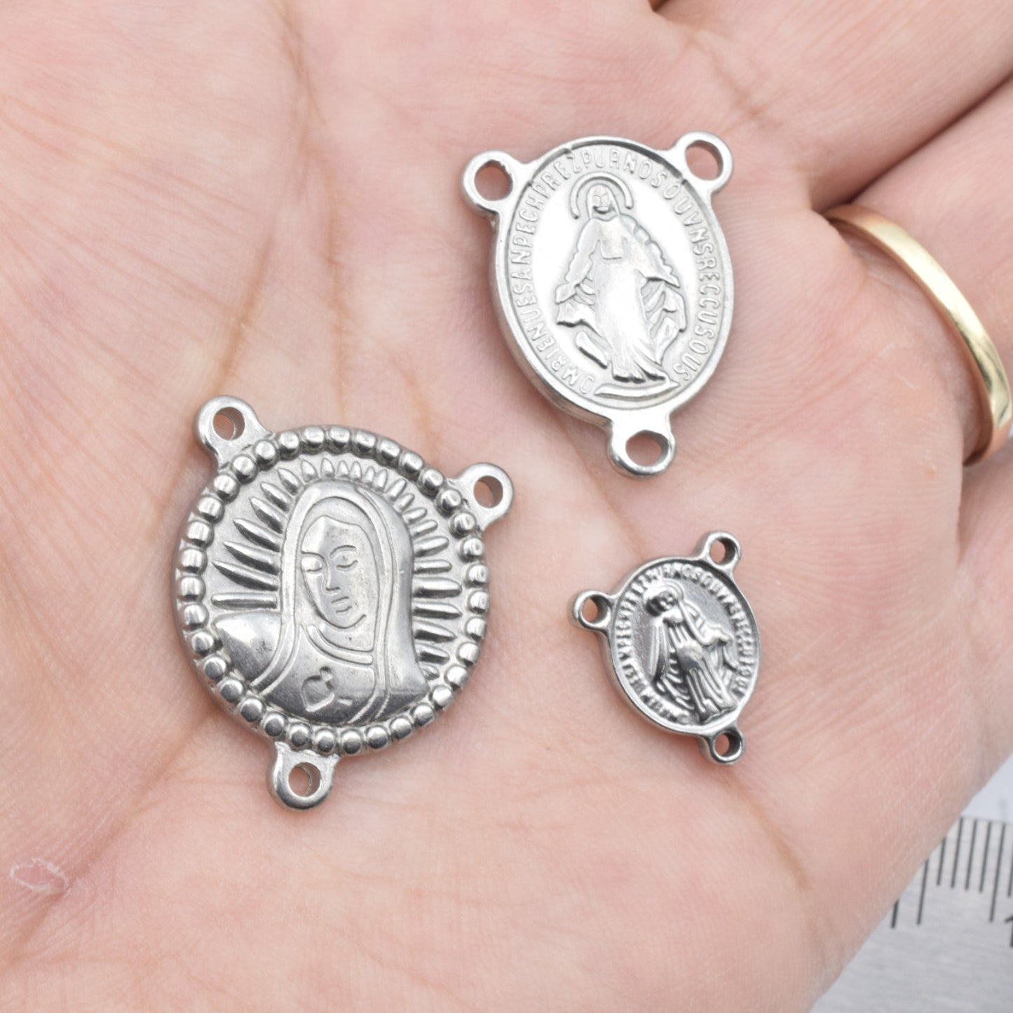 "Silver religious medallion connectors in hand, Virgin Mary design"