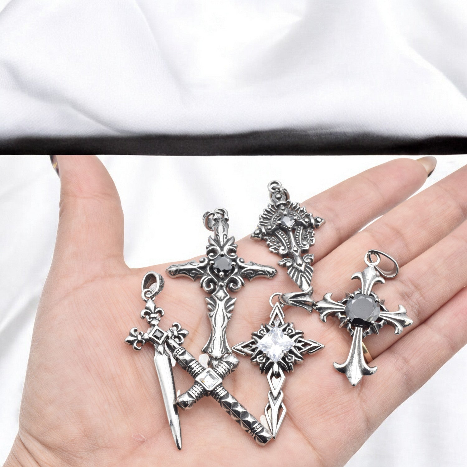 Hand holding five silver cross sword pendants with black gemstones.