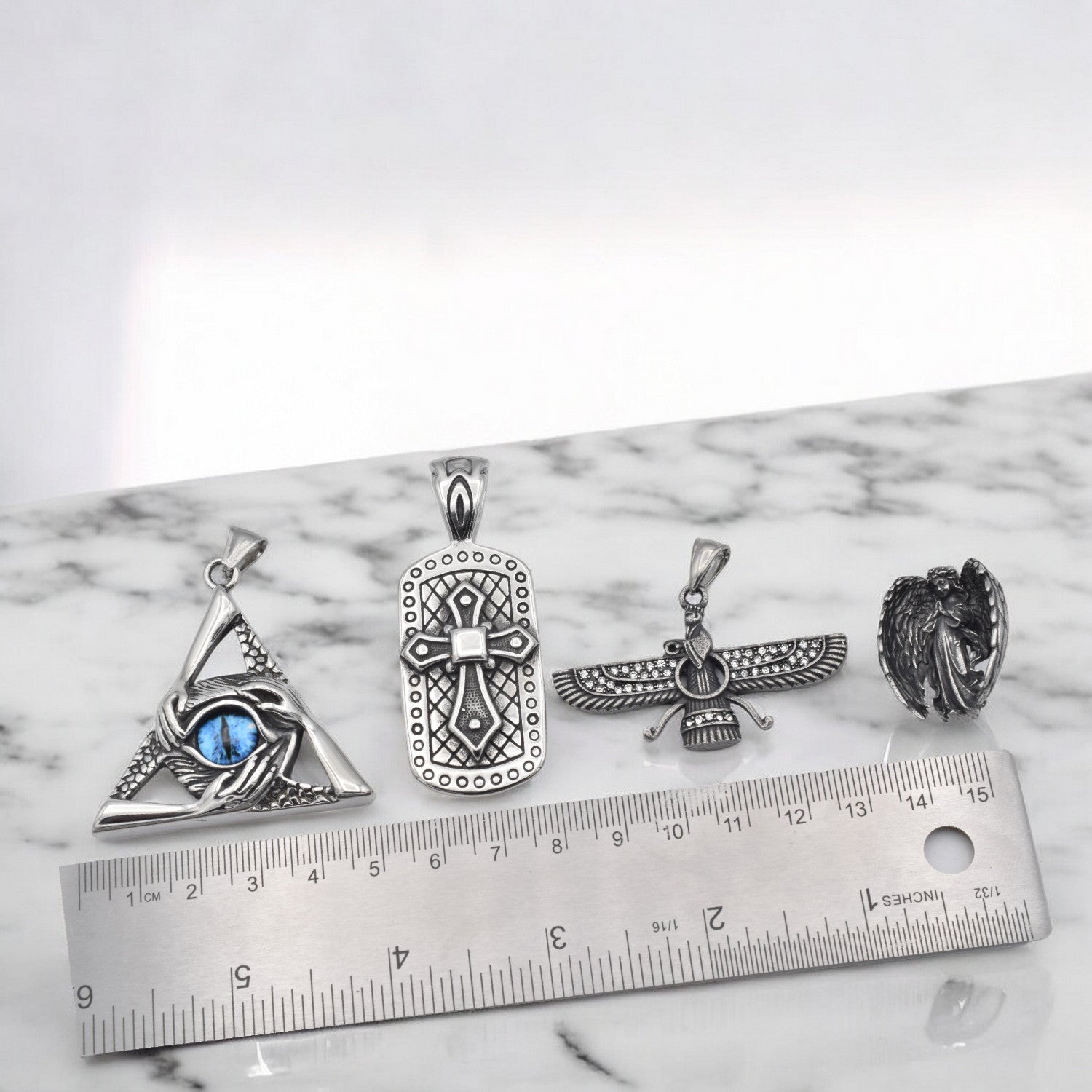 Various silver pendants with intricate designs on marble surface, including a ruler for scale.