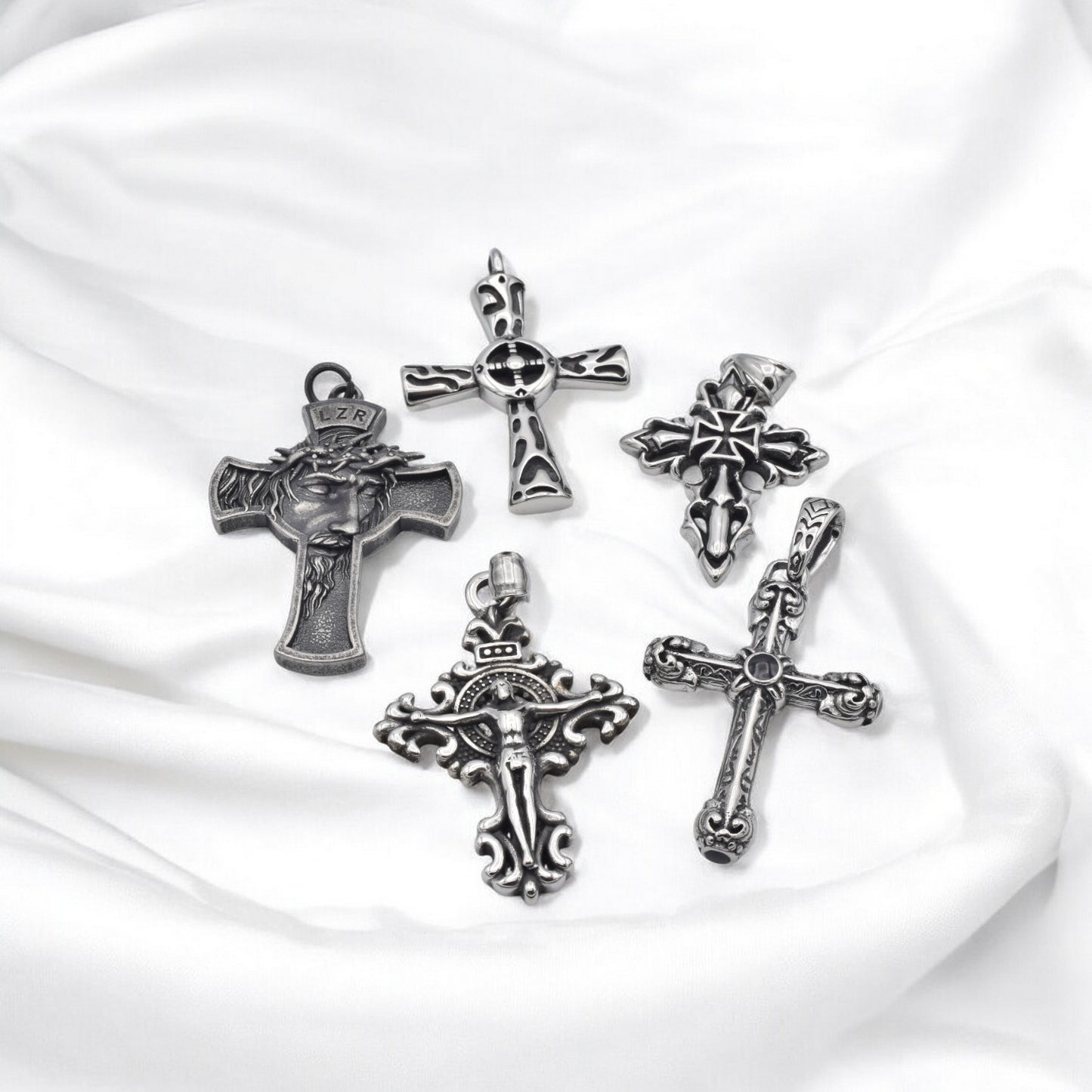 Silver cross pendants on white fabric background.