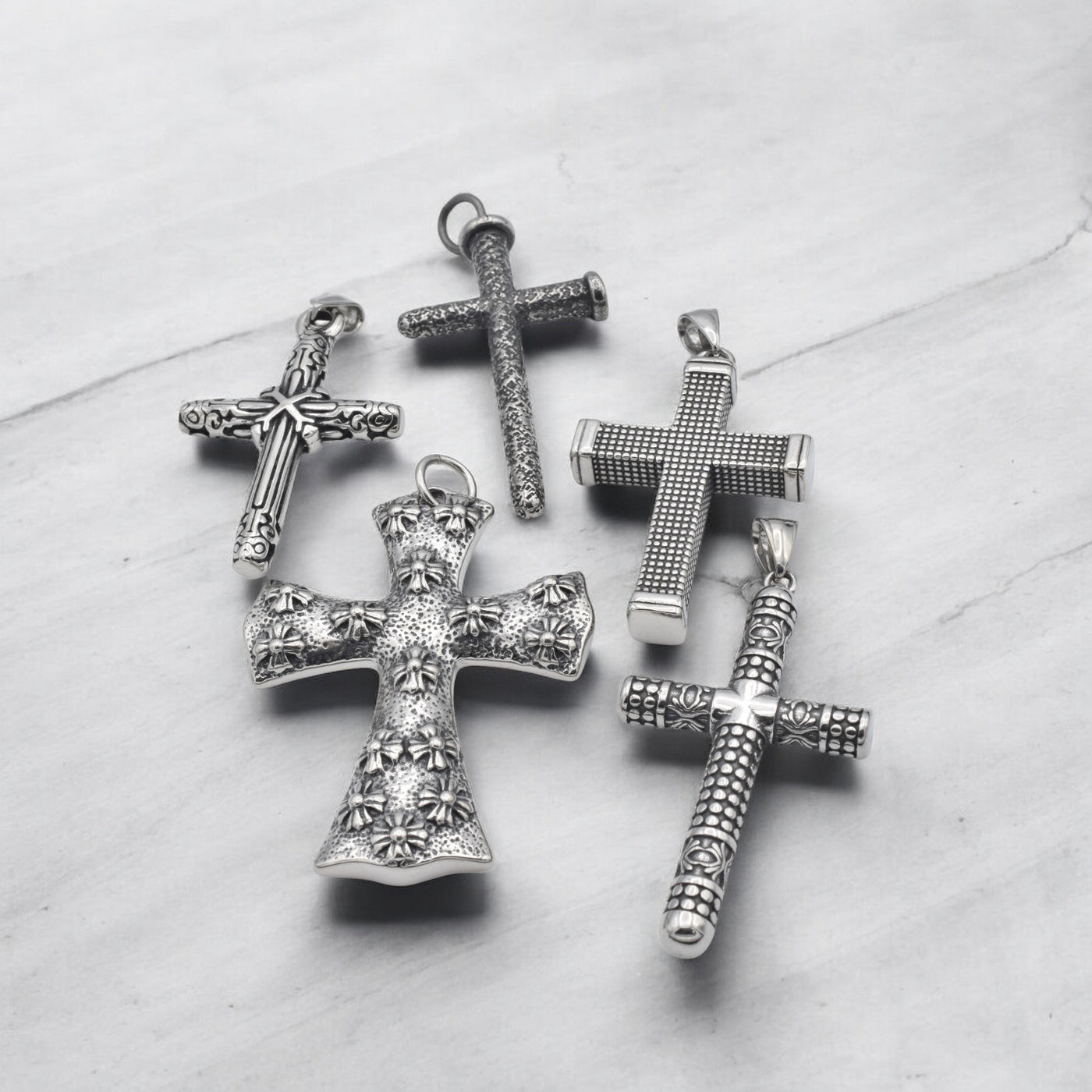 Vintage silver cross pendants with intricate designs on marble background.