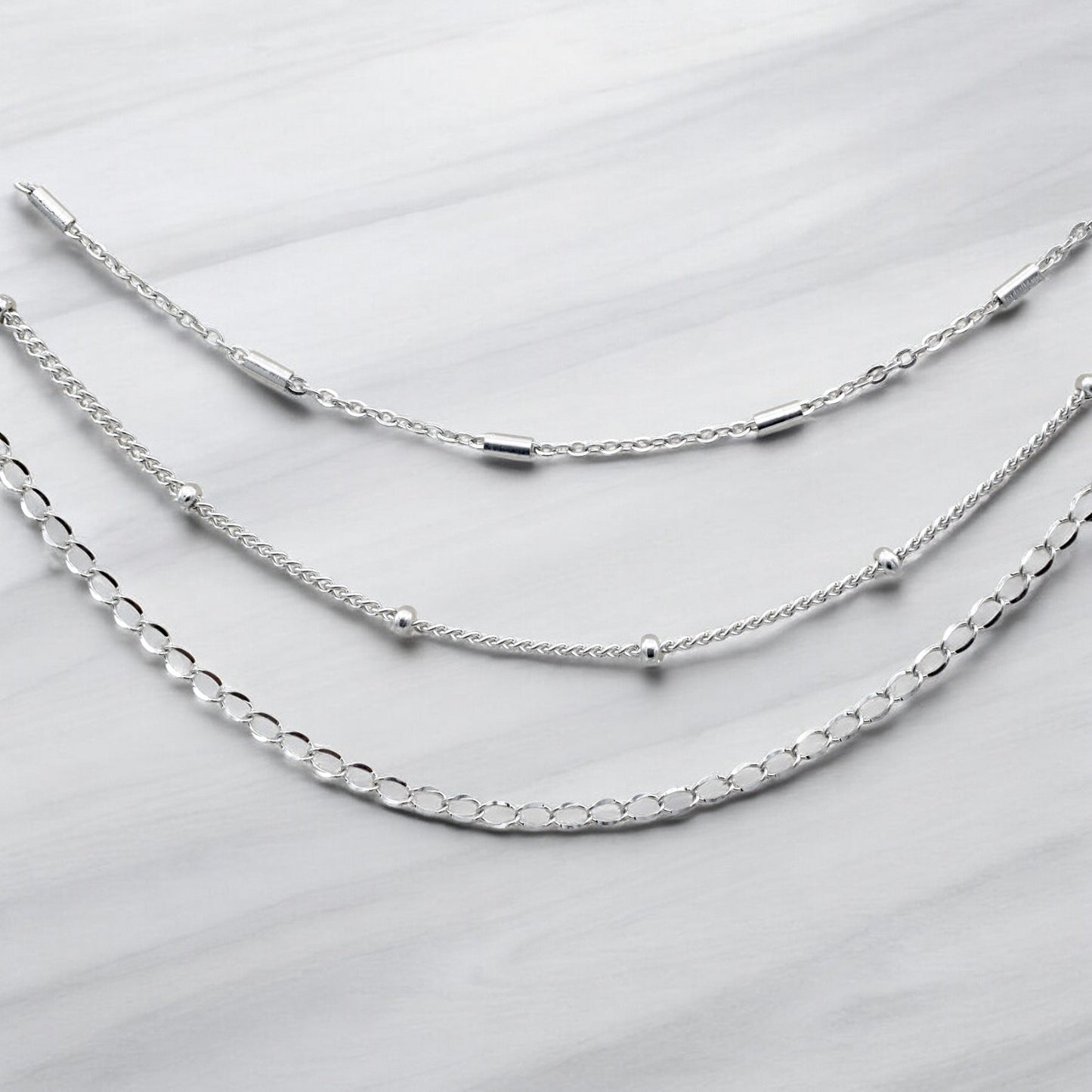 "Three layered silver chain necklaces on marble background"