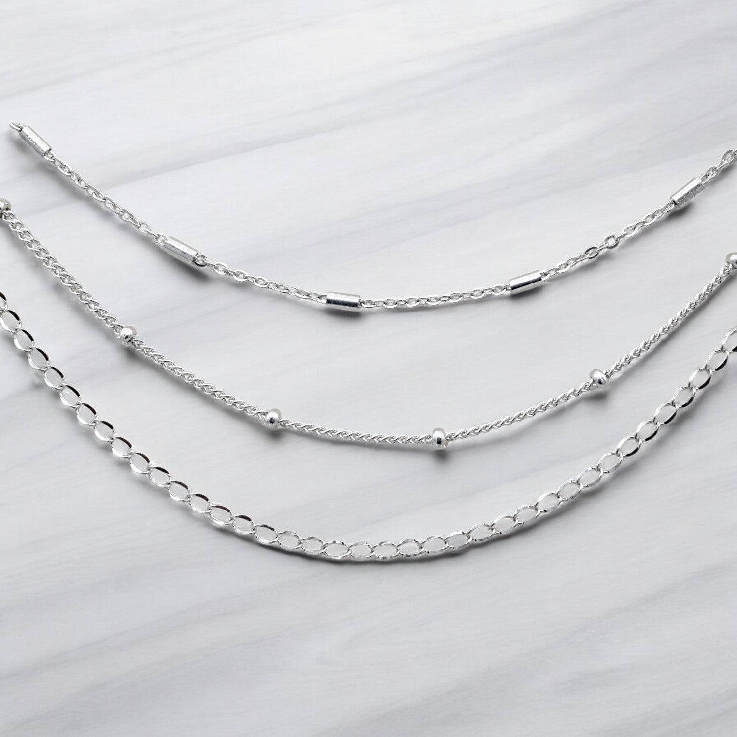 "Three layered silver chain necklaces on marble background"