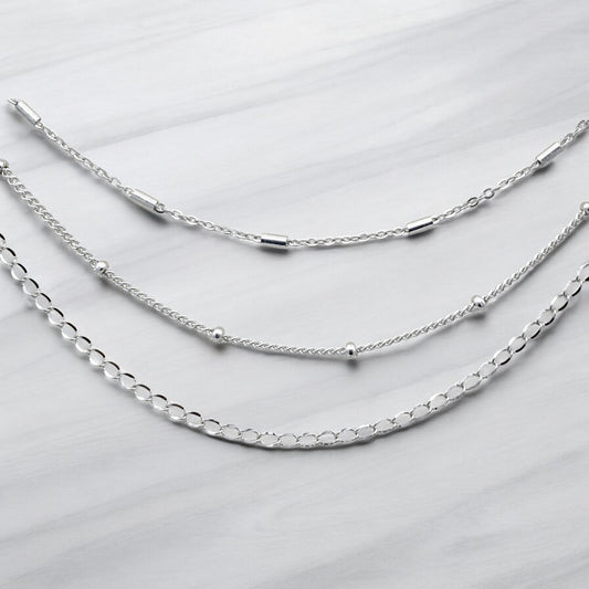 "Three layered silver chain necklaces on marble background"