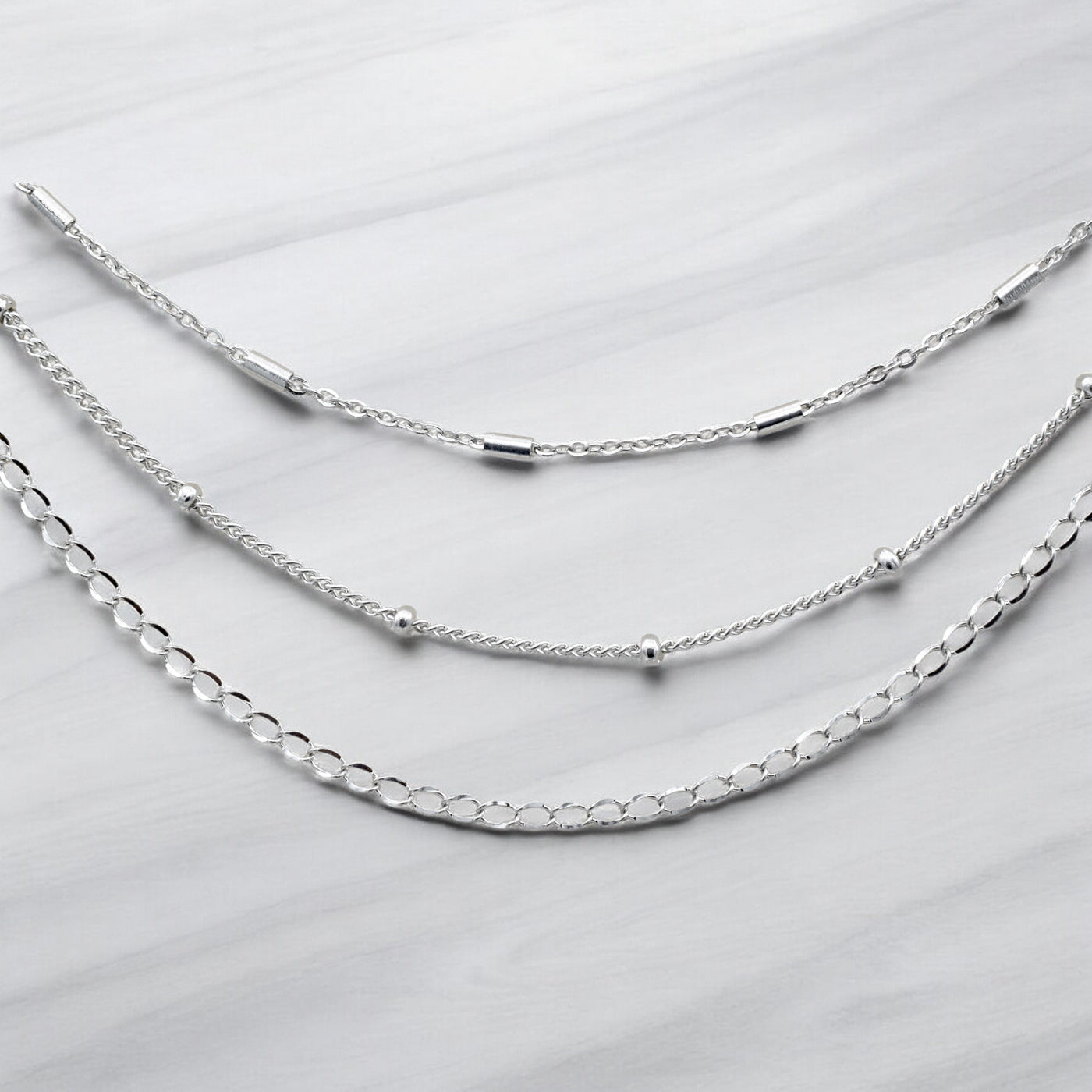 "Three layered silver chain necklaces on marble background"