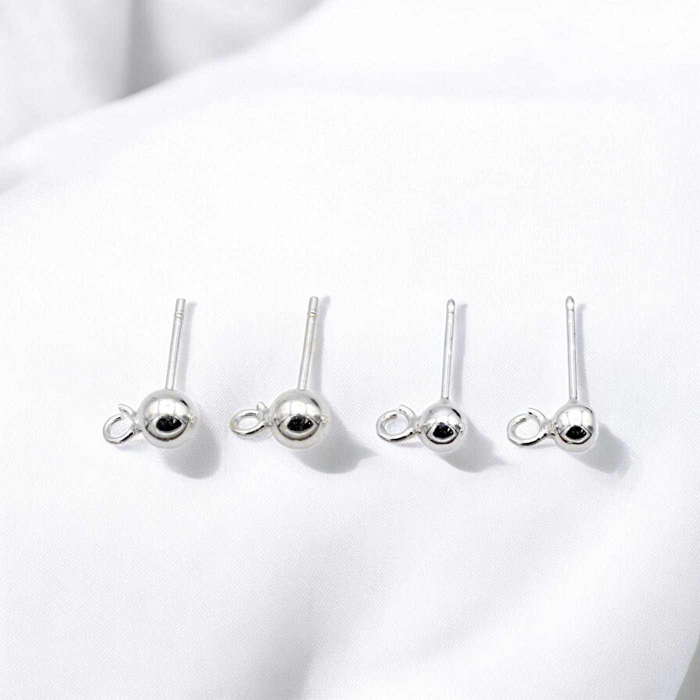 "Set of four silver ball stud earrings on white background"