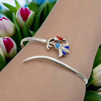 Silver cuff bracelet with multicolored gemstone flower design amidst tulips.