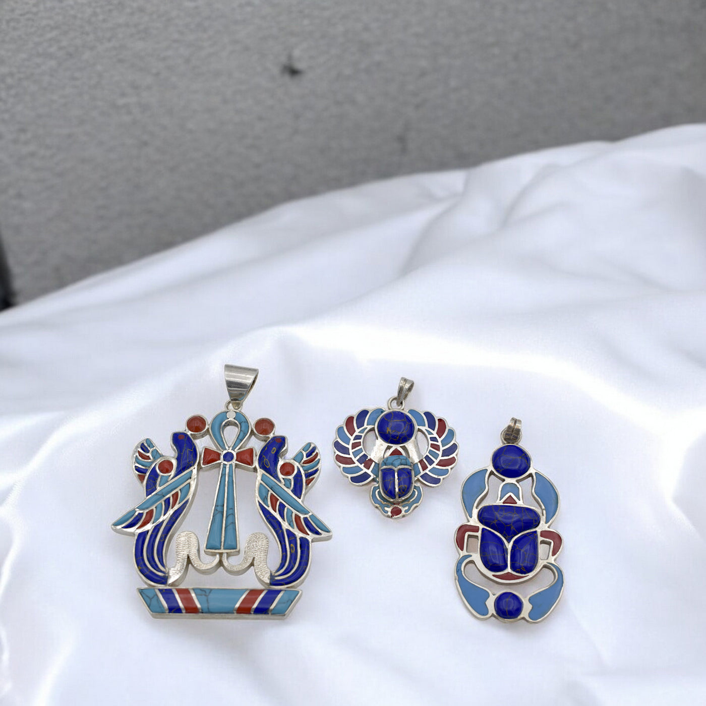 Silver and enamel Egyptian-inspired pendants on white fabric background.