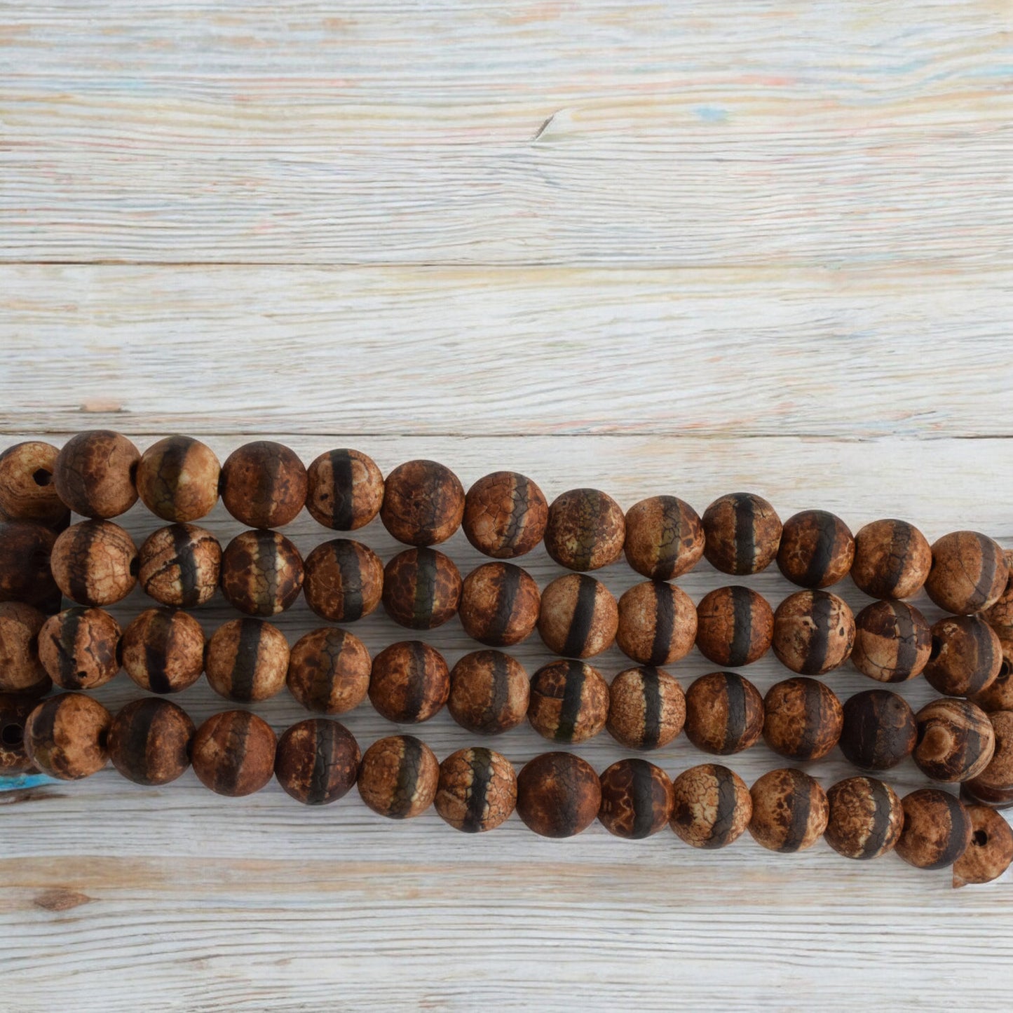 Brown striped gemstone beads on wooden background.