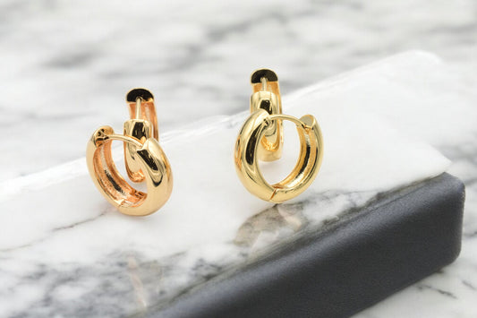 Gold hoop earrings on marble background.